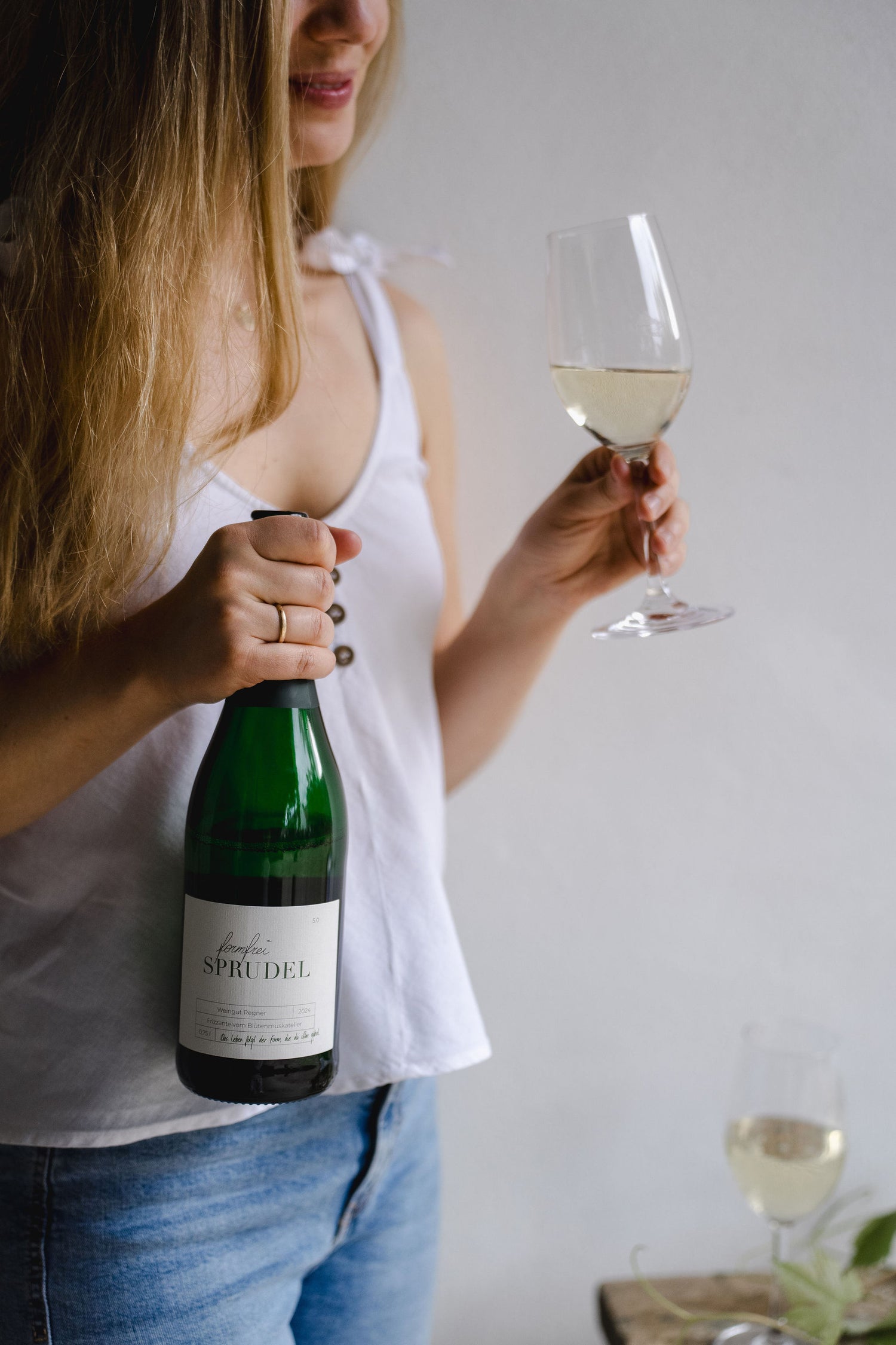 Frau hält Sprudel Flasche in der rechten hand und ein gefülltes Weinglas in der linken Hand. 